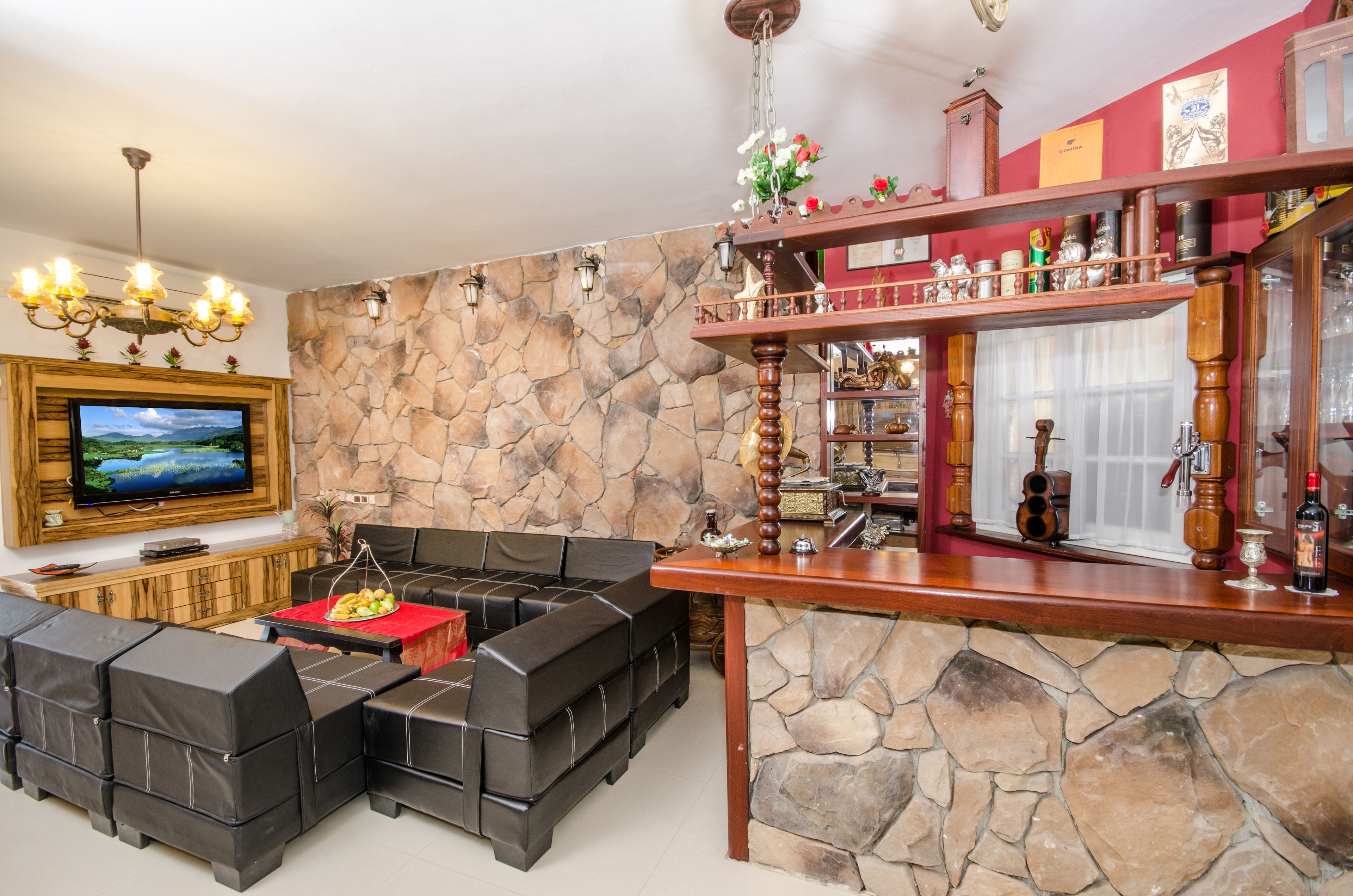 Una sala de estar con pared de piedra, barra de madera y televisor montado en la pared.