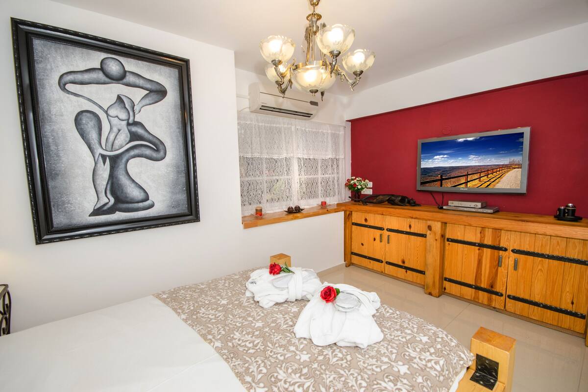 A hotel room with a bed, a painting, a television, a wooden cabinet, and two towels with roses.
