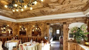 Een restaurant met houten lambrisering, ronde tafels en comfortabele zitbanken.