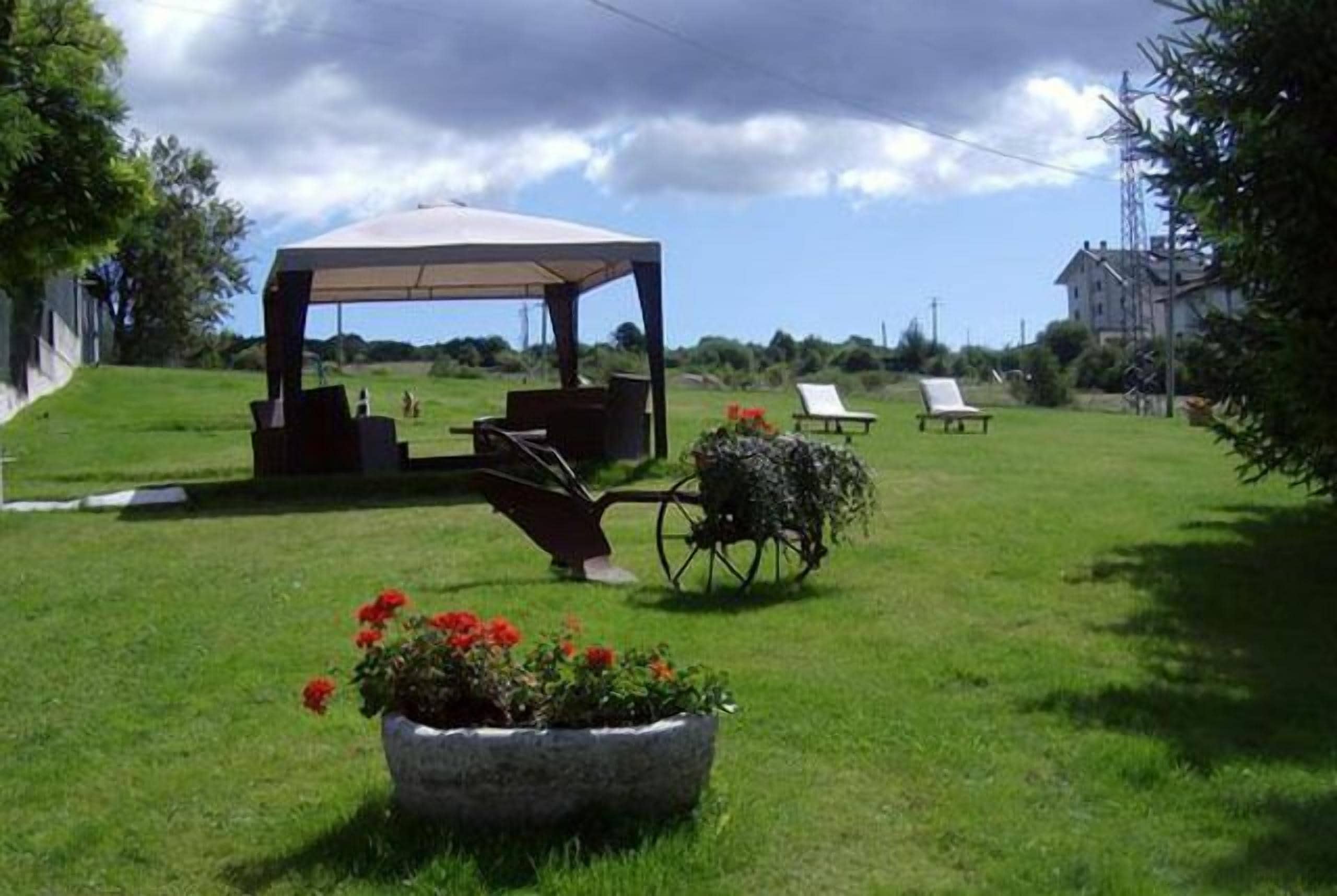 Un espacio exterior con un pabellón, sillas de jardín y una jardinera con flores rojas.