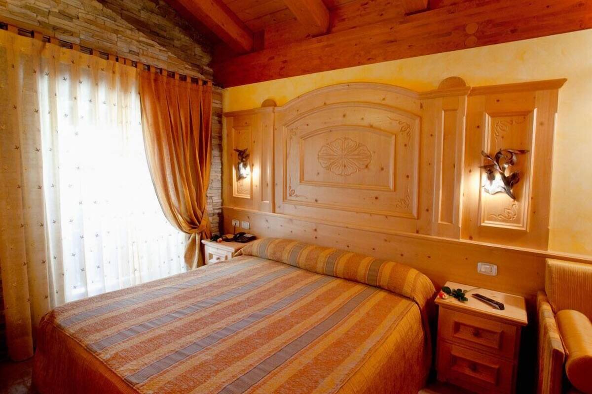 Un dormitorio con paneles de madera, una cama grande, una mesita de noche y una lámpara fijada a la pared.