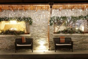 Un rincón al aire libre acogedor con dos sofás de mimbre, una pared de piedra y luces festivas.