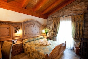 Un dormitorio con cabecera de madera, una cama con colcha estampada, una mesita de noche con lámpara y una ventana con cortinas.