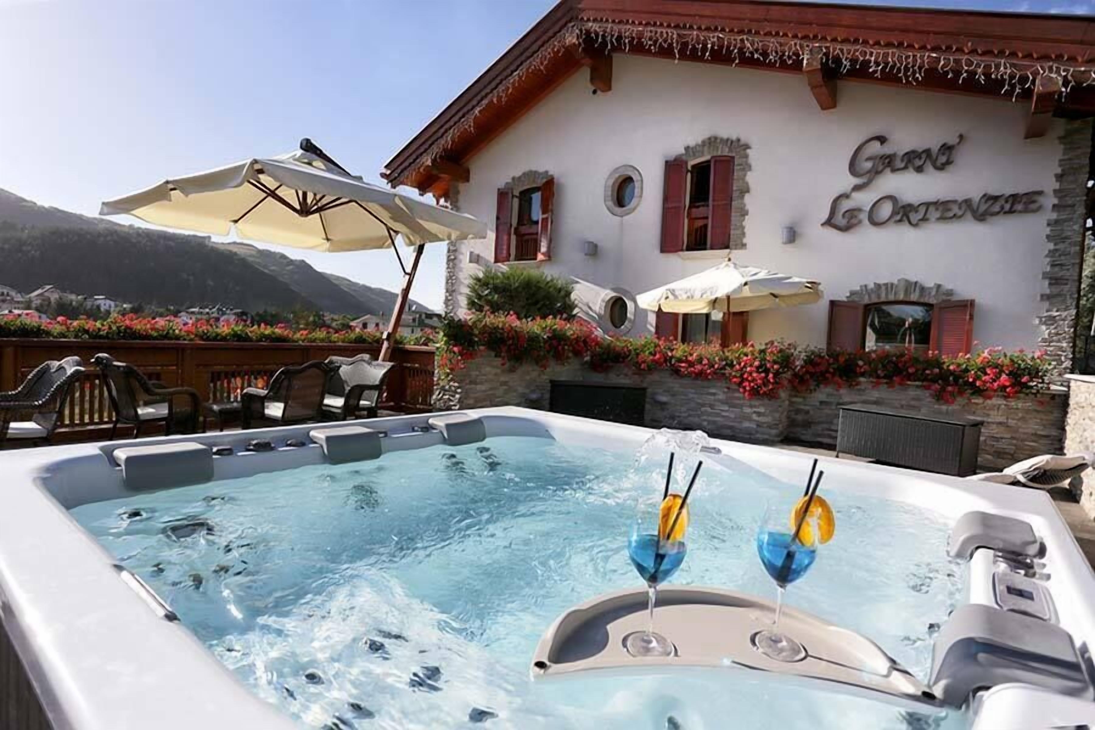 A hot tub with two drinks, outdoor seating, and a building with 'Garni Leontzien' signage.
