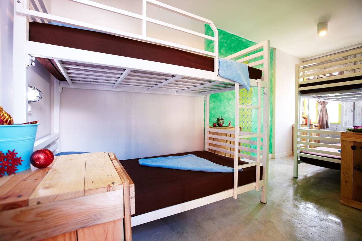A bunk bed room with a wooden desk and a blue bucket.