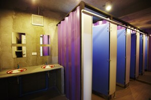 A restroom with two sinks, a mirror, and a row of stalls. - WH Hostel (Bangkok)