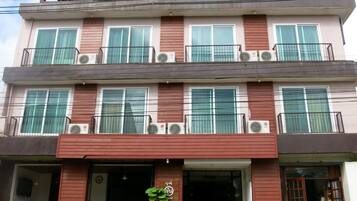 A multi-story building with balconies, air conditioning units, and a front entrance with outdoor seating.