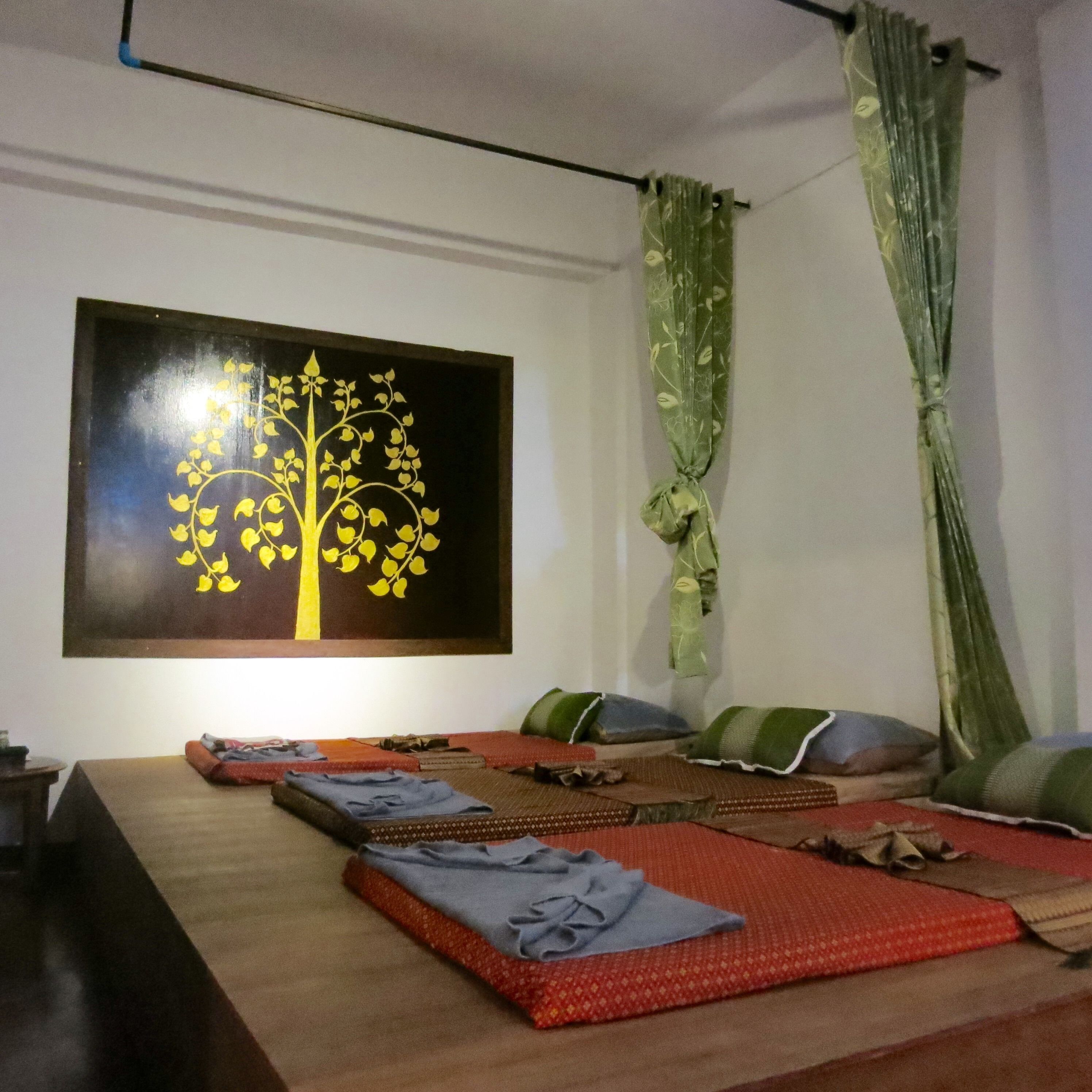 A room with a bed, pillows, a blanket, and a painting of a tree on the wall.