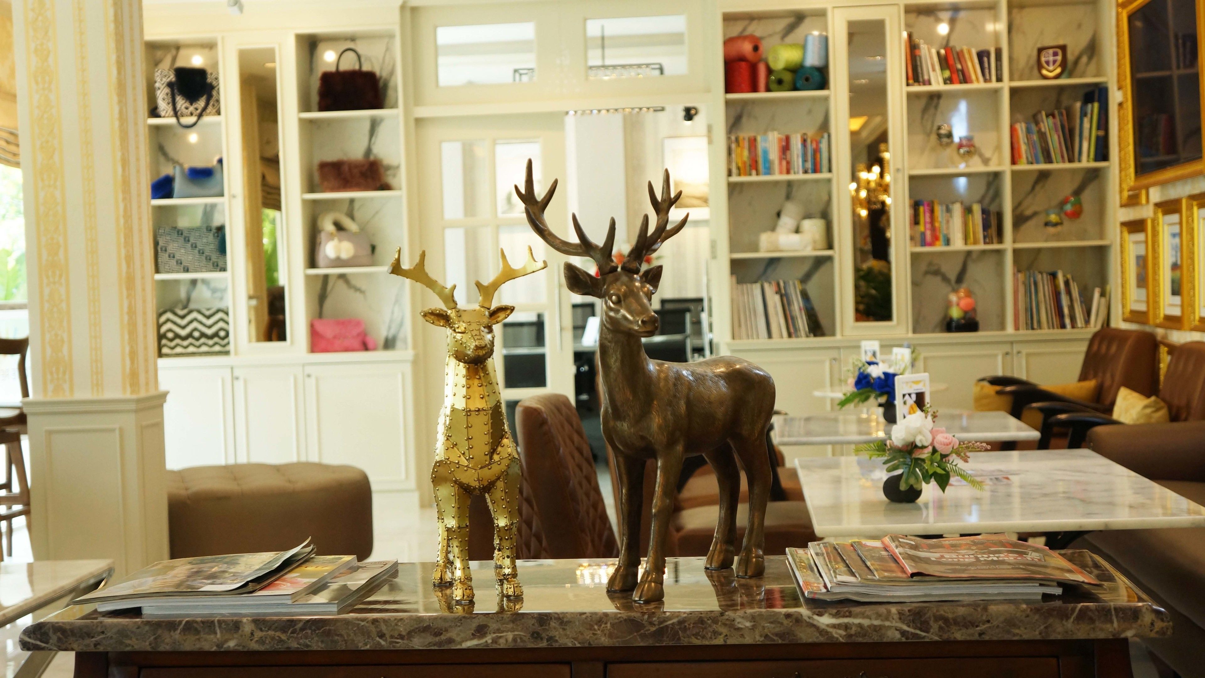A room with a marble countertop displaying two deer figurines, a bookshelf with books, and a dining area with a table set for two.