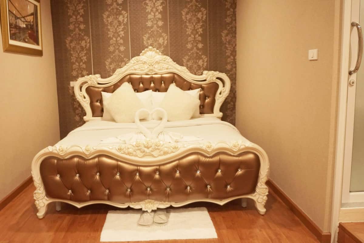 A bed with a tufted headboard, white bedding, and a heart-shaped decoration on the bedspread.