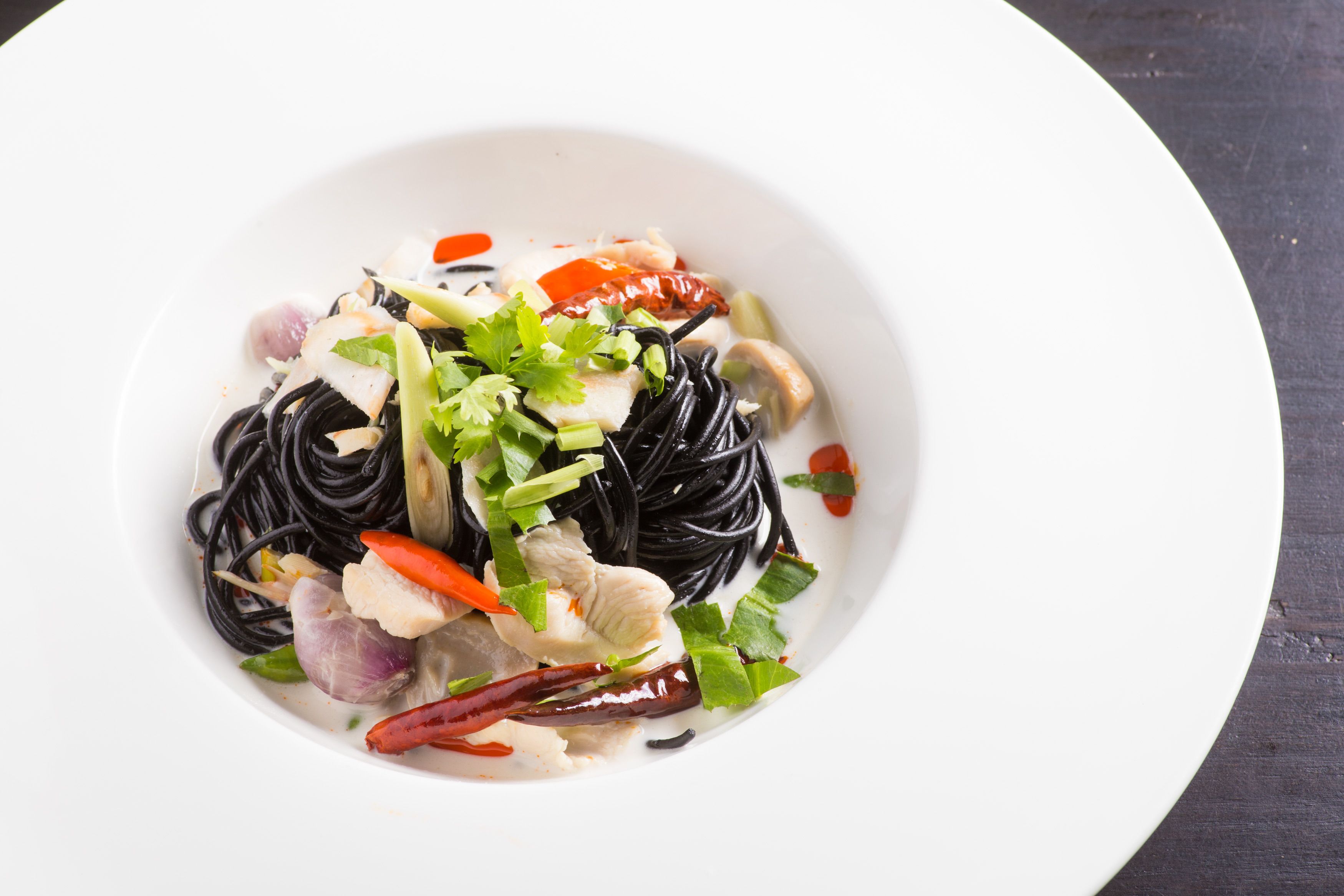 A bowl of black noodles with vegetables and fish on a white plate.