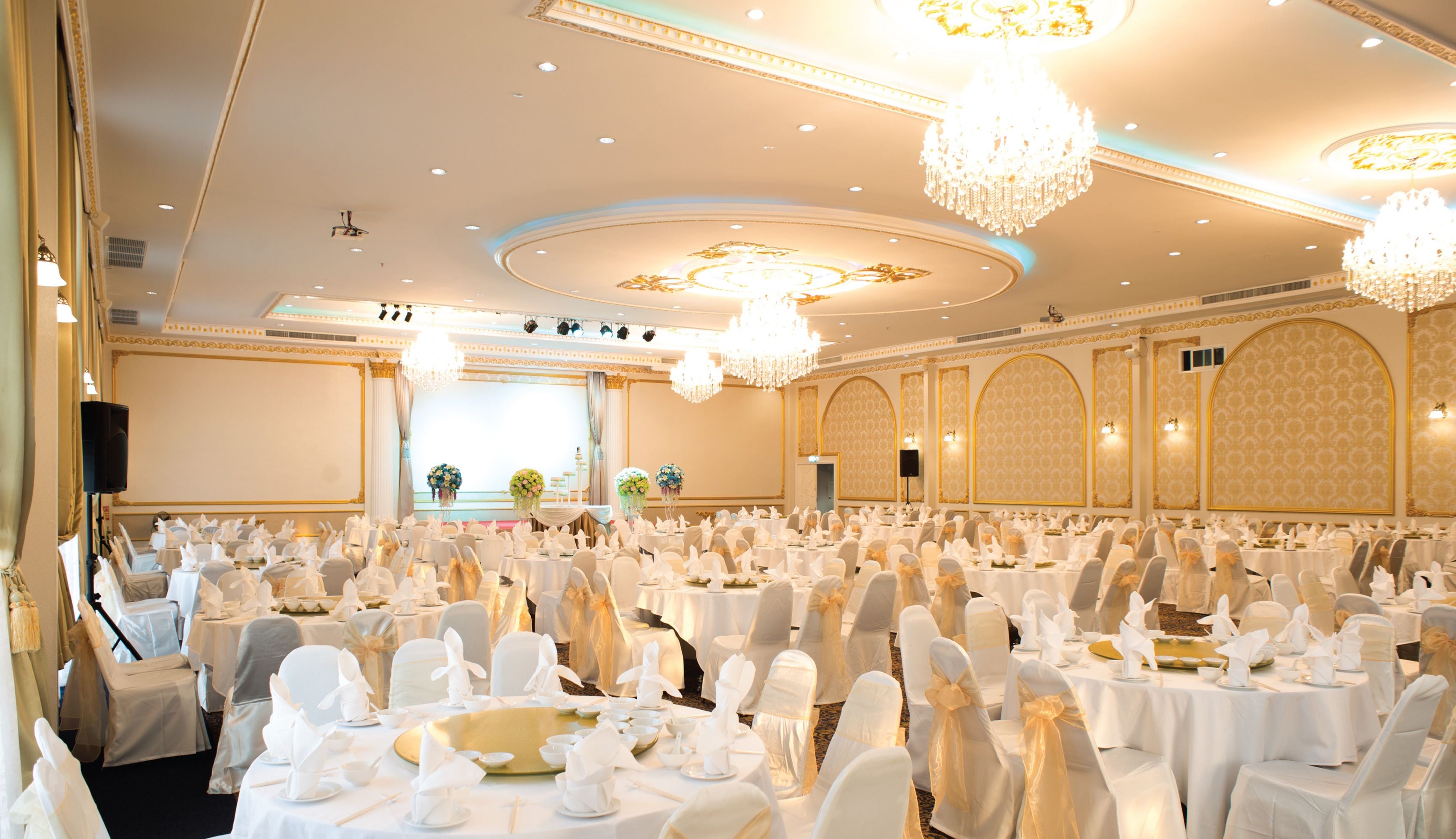 A banquet hall with round tables, white tablecloths, and chairs with white covers.