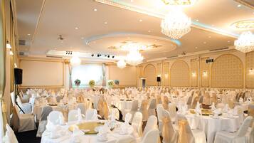 A banquet hall with round tables, white tablecloths, and chairs with white covers.