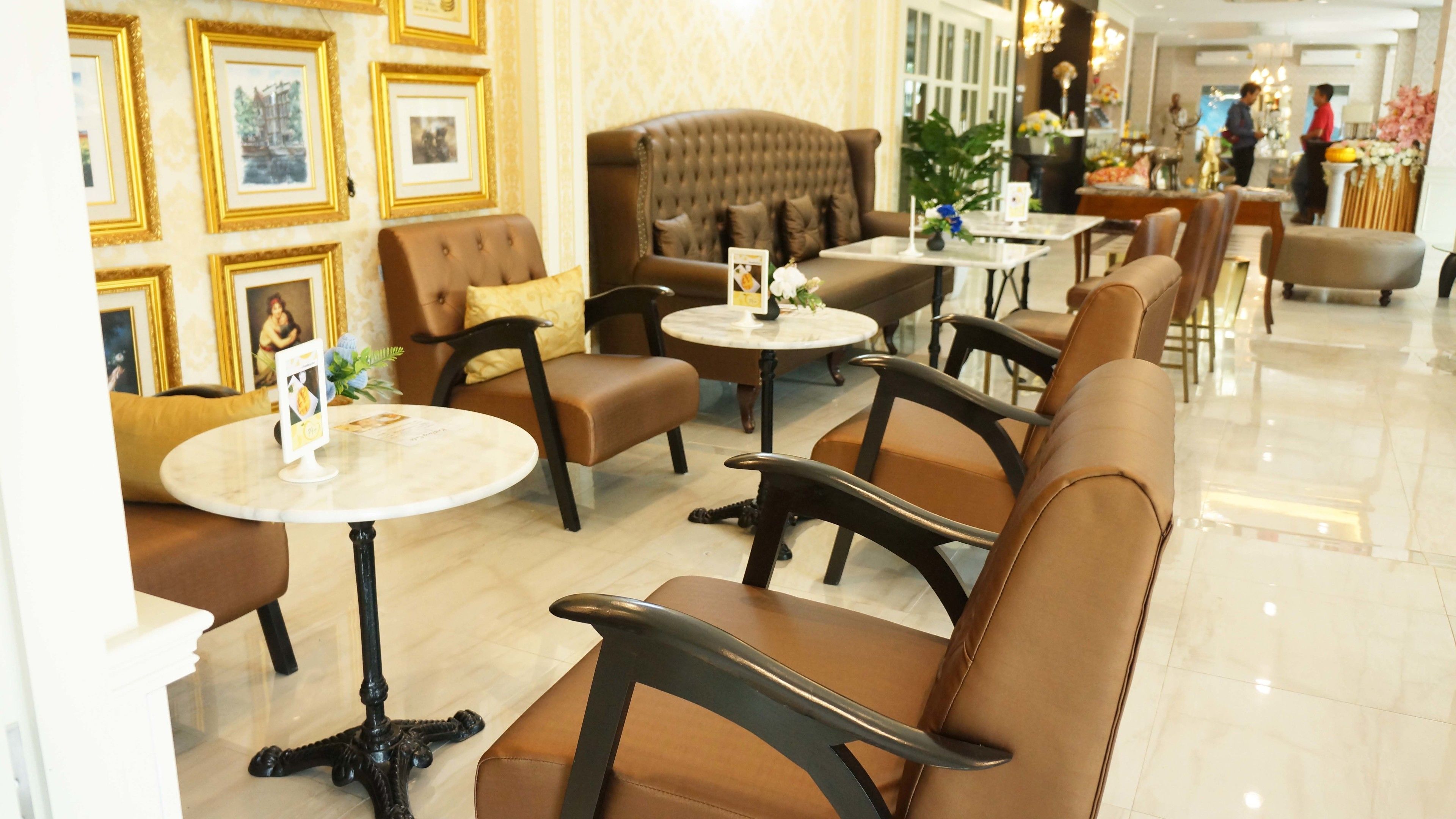 A hotel lobby with leather sofas, round tables, and framed pictures on the walls.
