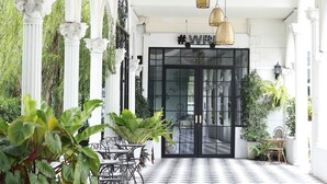 A covered outdoor area with a checkered floor, white columns, and outdoor seating. - Westgate Residence Hotel (Bang Yai)