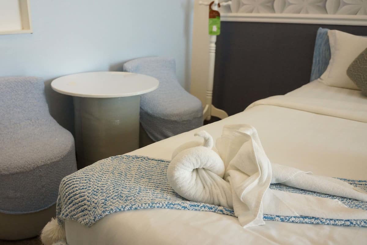 A hotel room with a bed, two grey armchairs, a small round table, and a towel on the bed.