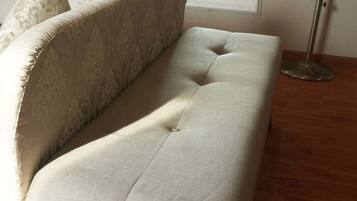 A room with a sofa, a door, a window, and a floor lamp.