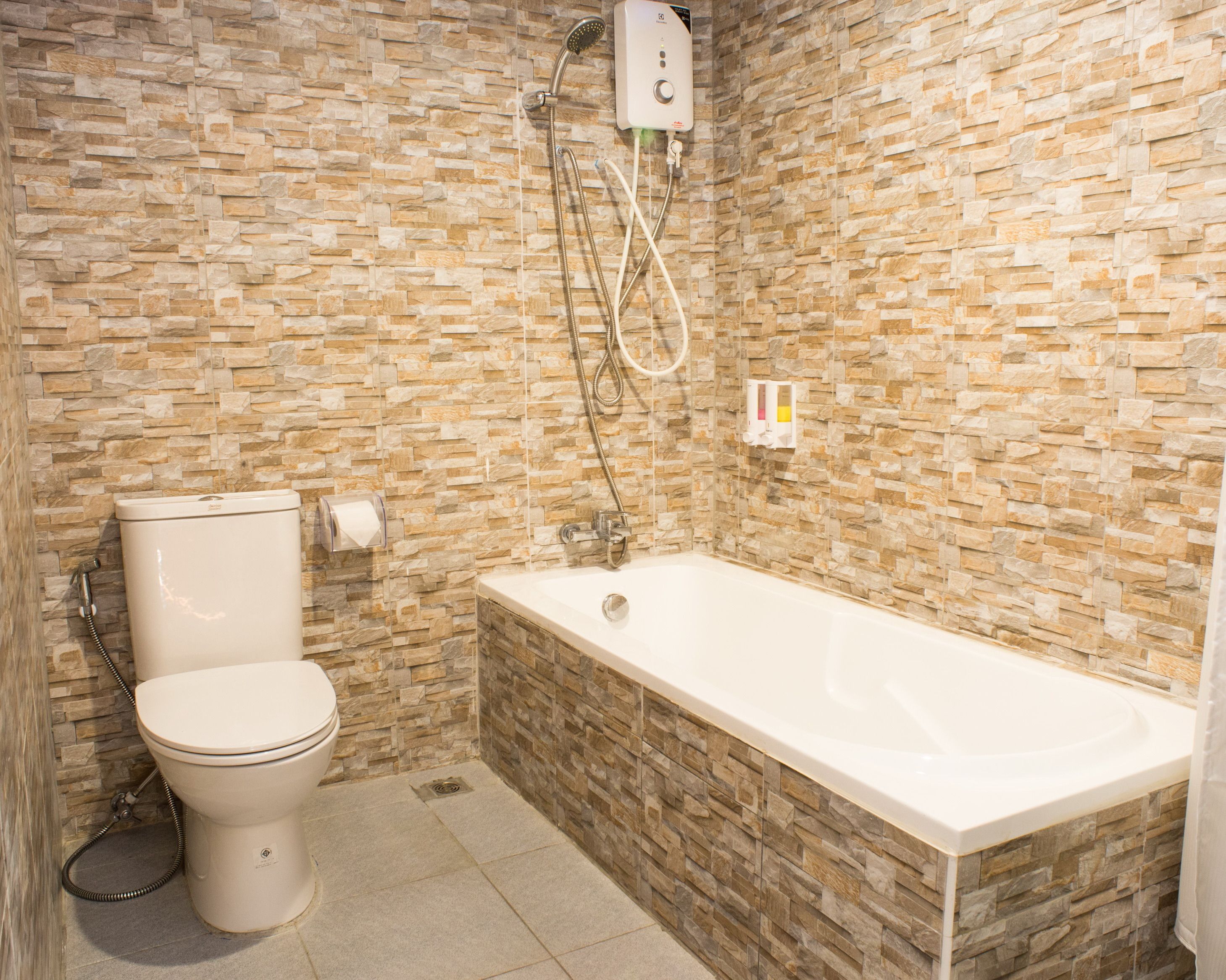 A bathroom with a stone wall, a toilet, and a bathtub.