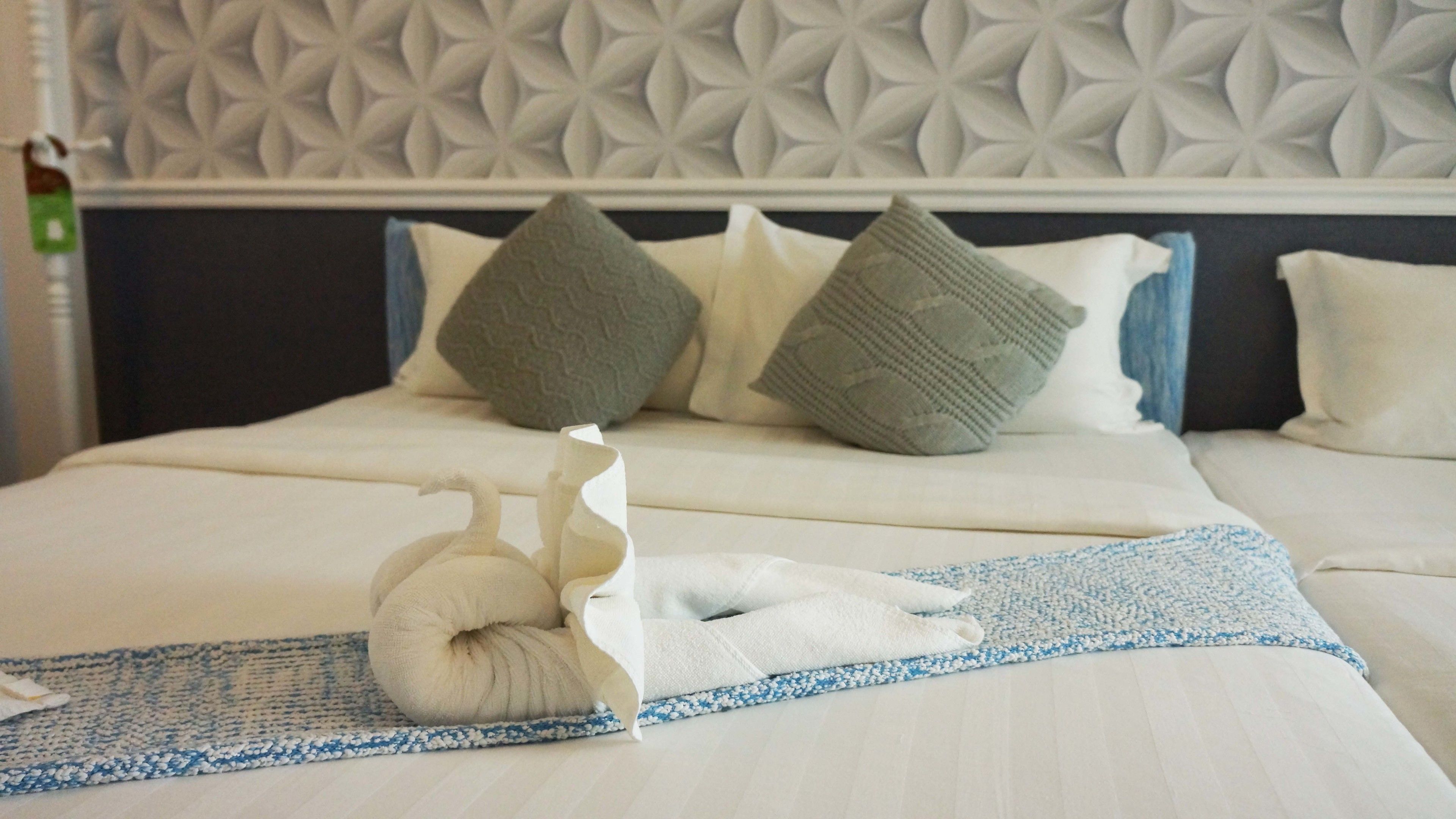 A neatly made bed with a patterned headboard, pillows, and a folded towel on a blue and white striped blanket.