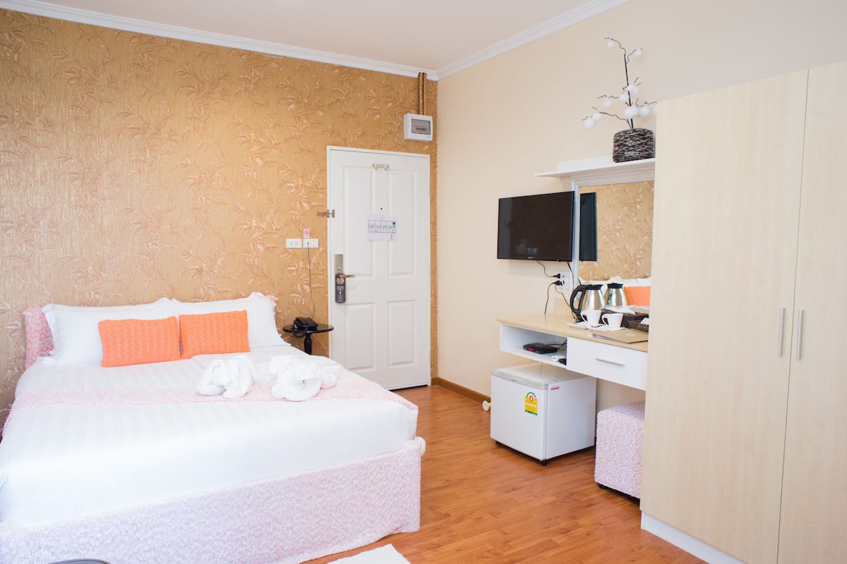 A bedroom with a bed, a television, a small kitchenette, and a wardrobe.