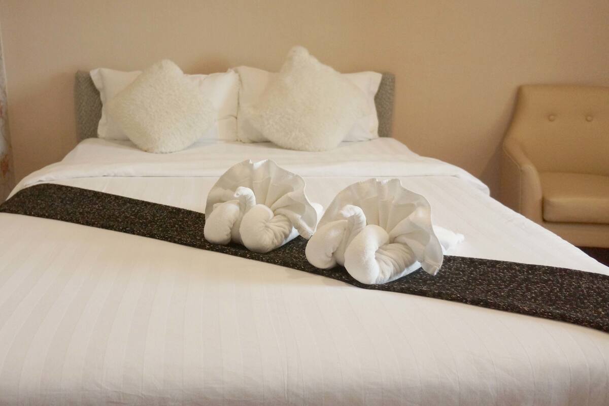 A neatly made bed with white linens, two pillows, and a decorative towel arrangement.