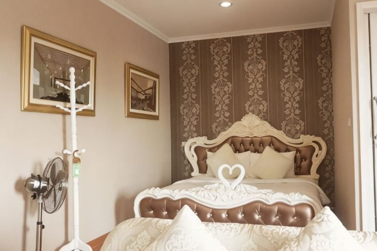 A bedroom with a large bed, a bedside table, and a wall-mounted fan.