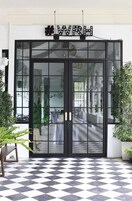 Entrada de hotel com chão xadrez em preto e branco, porta de vidro refletindo o interior e um letreiro acima da porta.