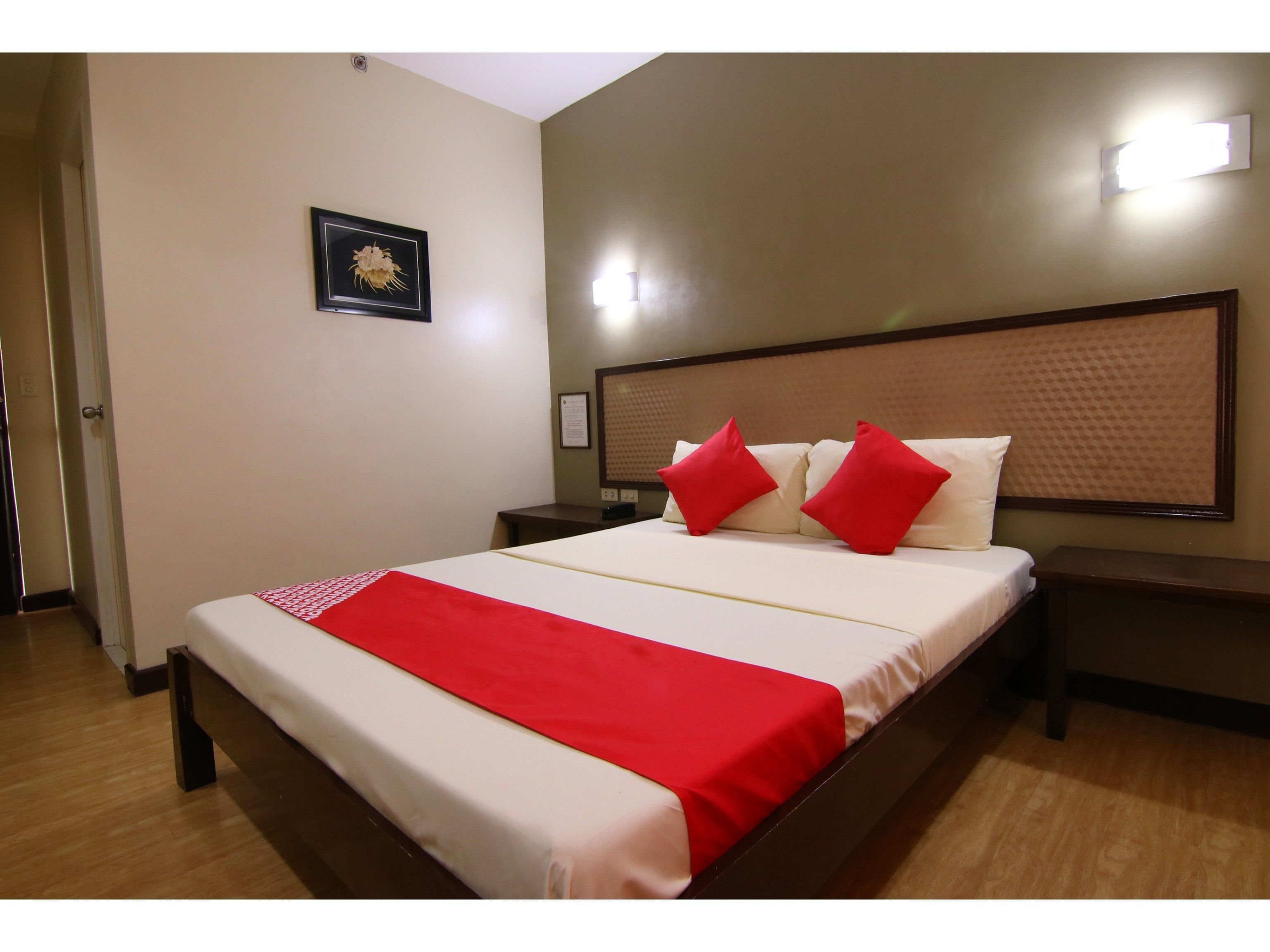 Una habitación de hotel con una cama grande, ropa de cama roja y blanca, y un cabecero de madera.