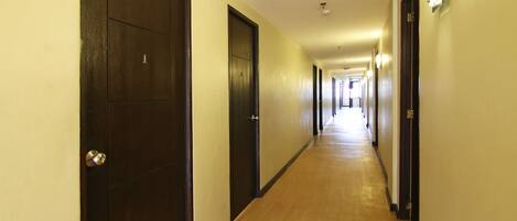 A long, narrow hotel corridor with wooden flooring and dark doors on both sides.