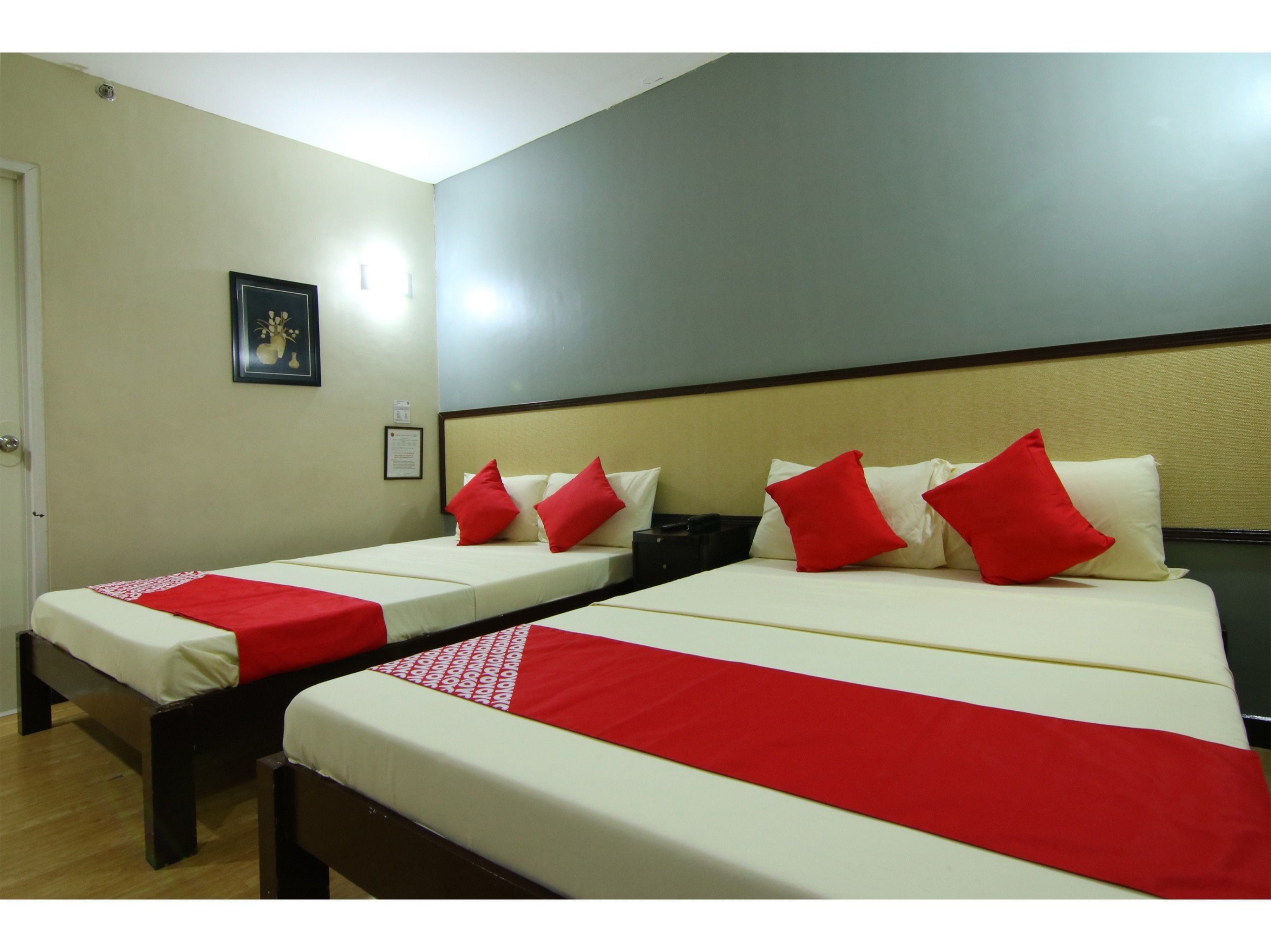 Habitación de hotel con dos camas individuales, cada una con una colcha roja y blanca, y cabeceros con estructura de madera.