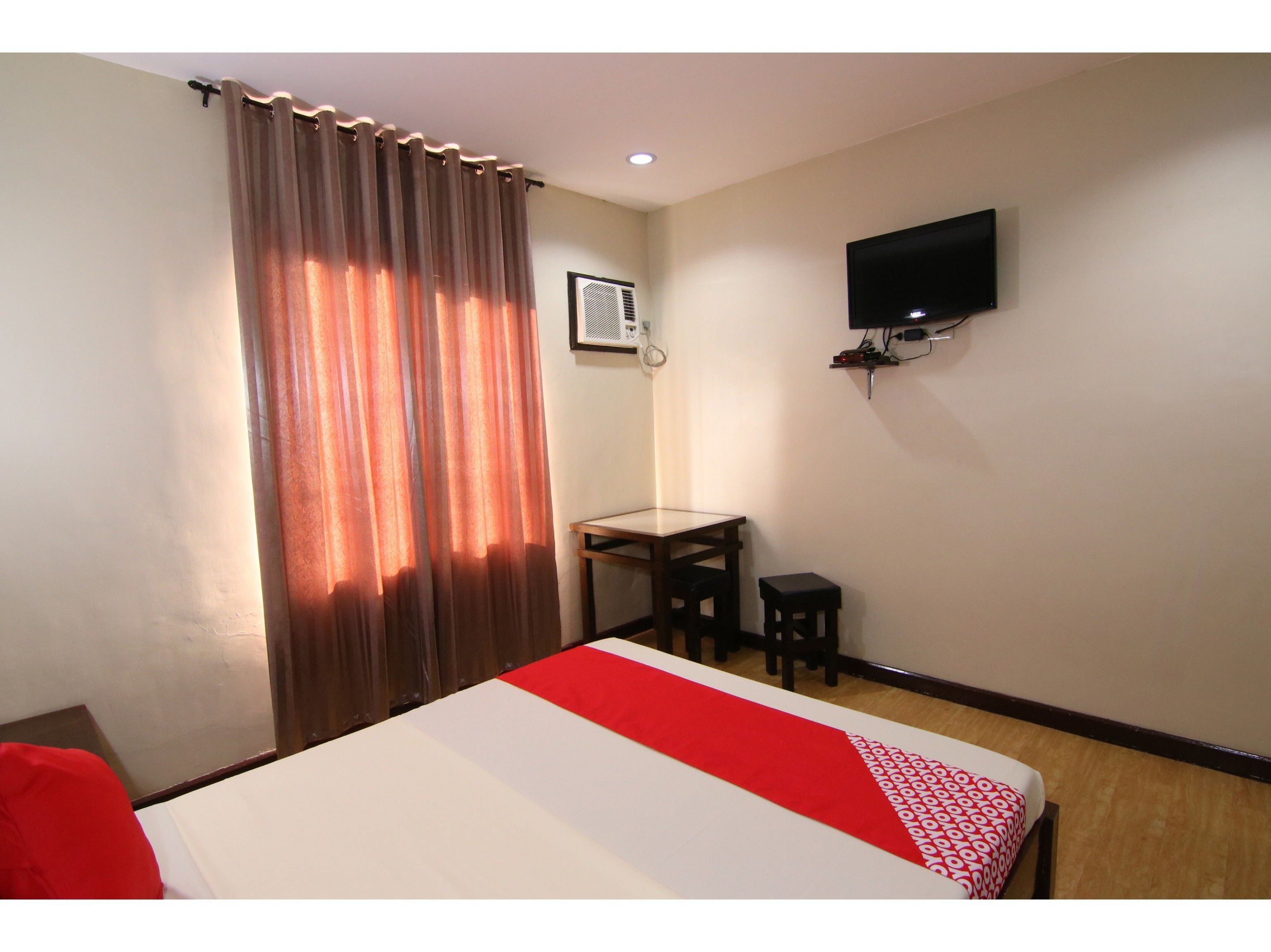Ein Hotelzimmer mit Bett, Schreibtisch, Stuhl, Fernseher und Vorhang.