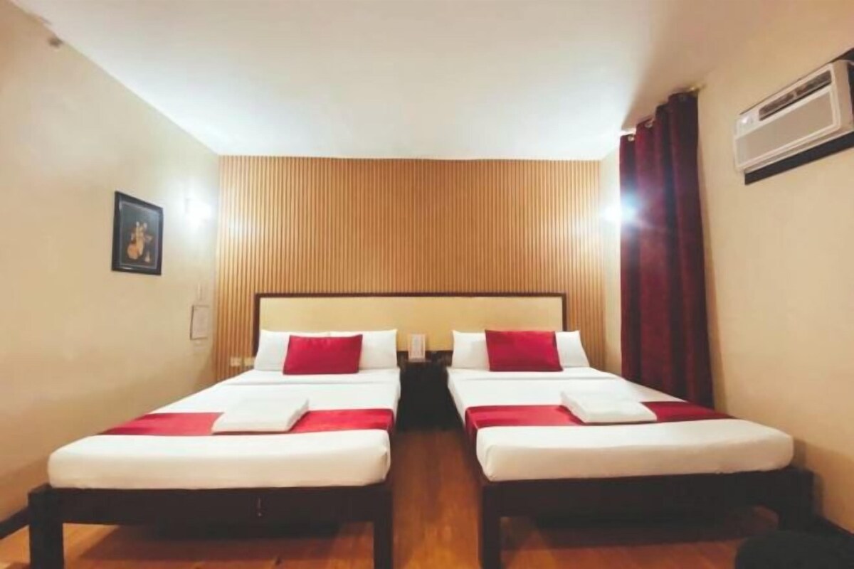 A hotel room with two beds, a wooden headboard, a red curtain, and an air conditioning unit.