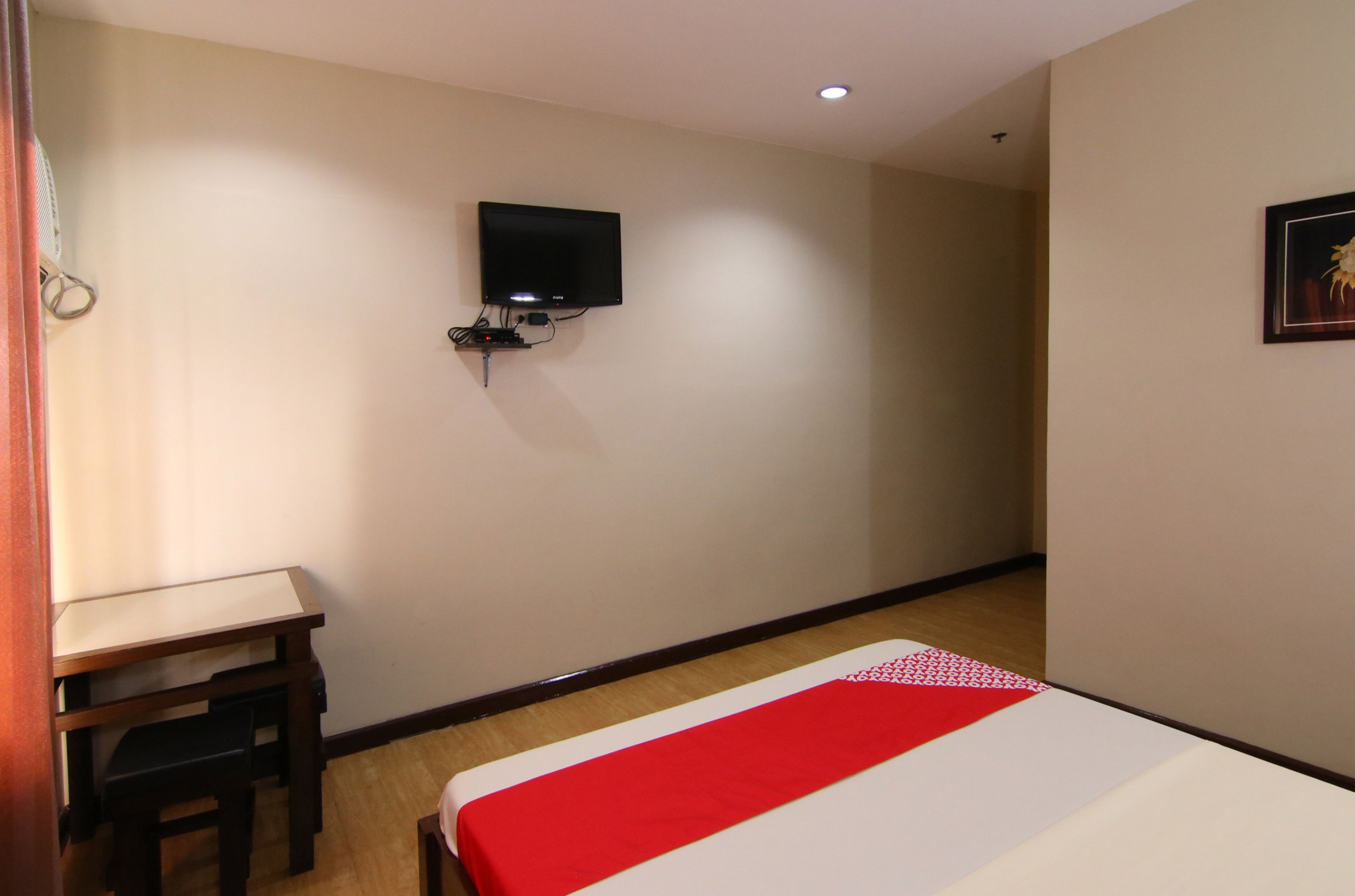 A hotel room with a bed, a desk, a television mounted on the wall, and a framed picture on the wall.