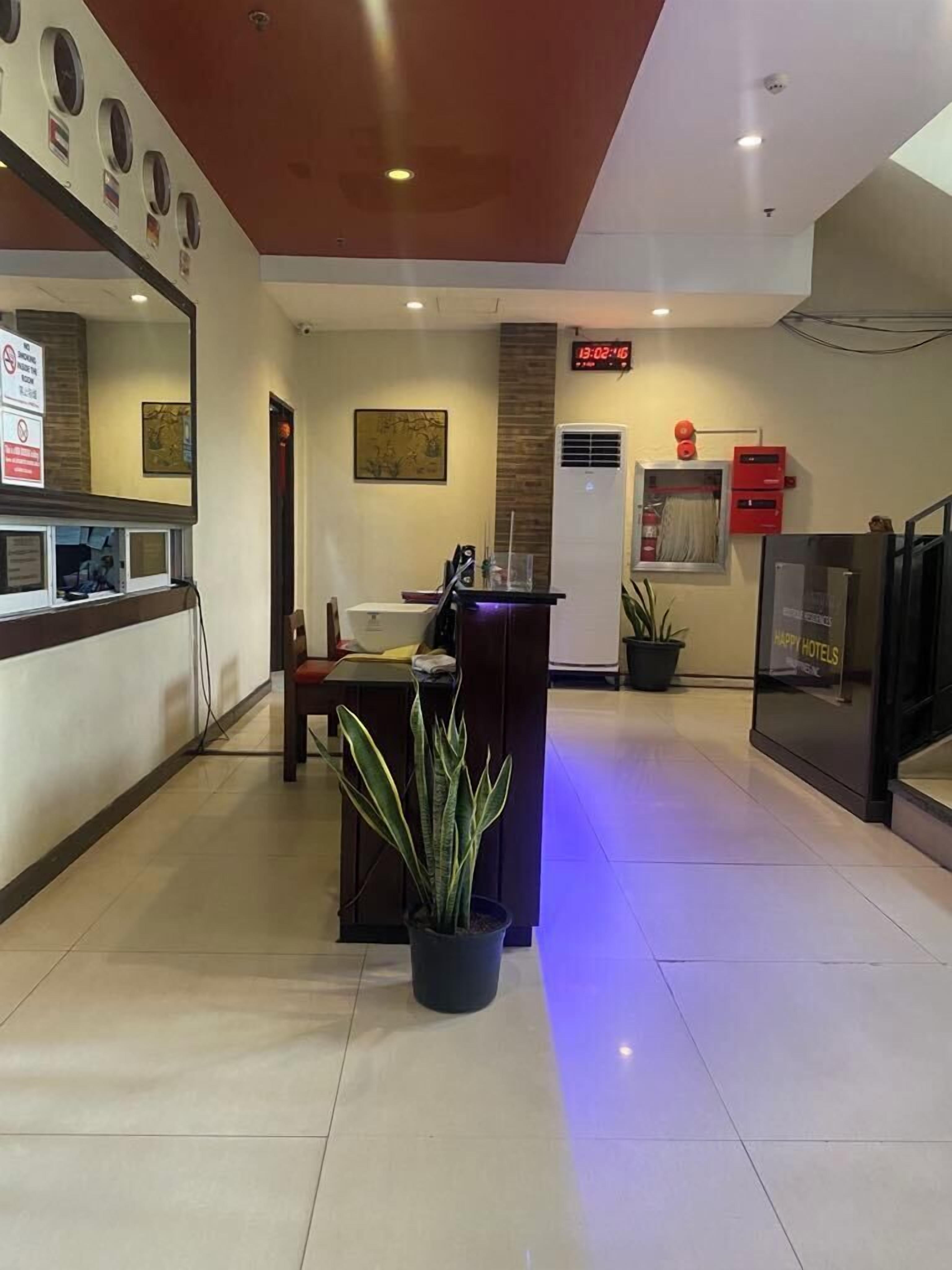 A hotel reception area with a reception desk, a digital clock, and a plant.