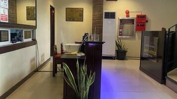 A hotel reception area with a reception desk, a digital clock, and a plant.