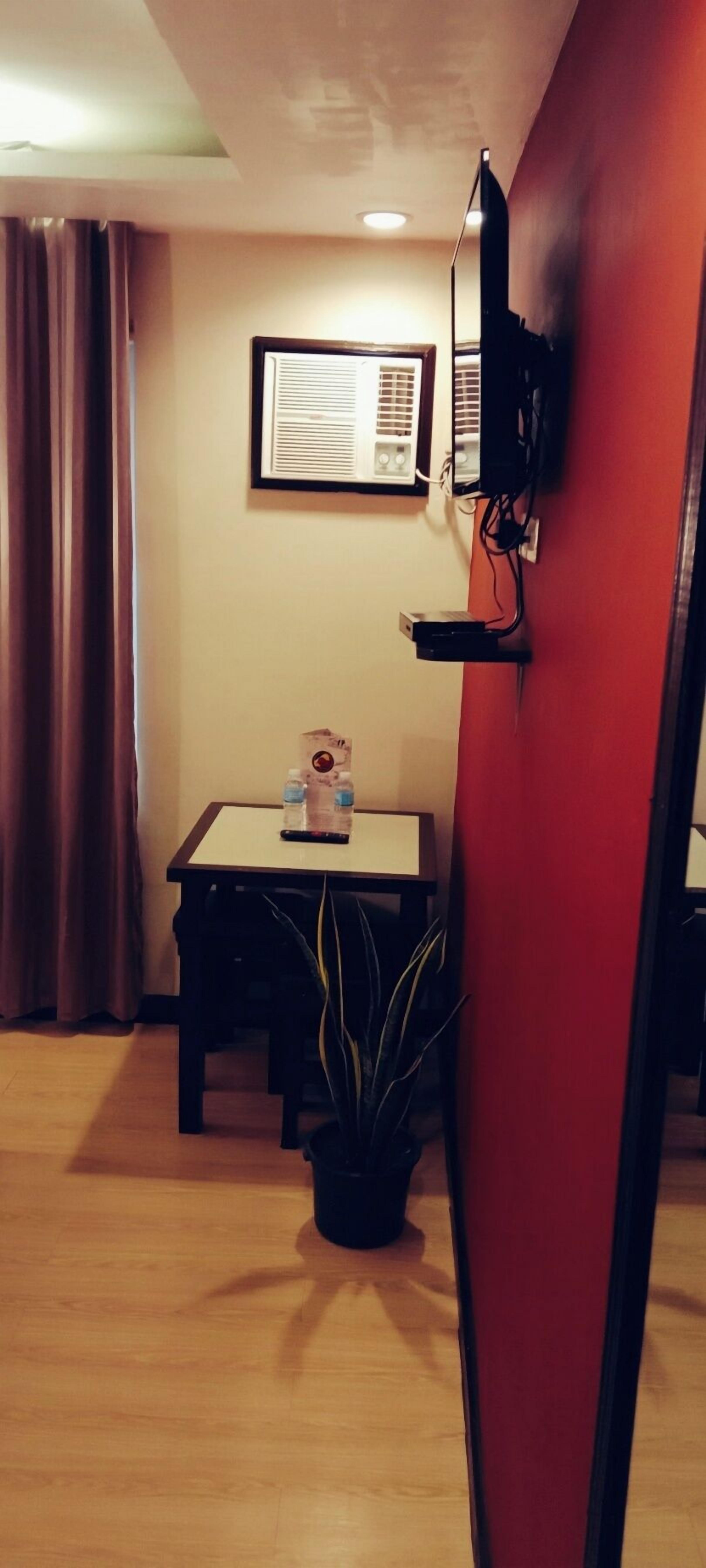 A room with a wooden floor, a table with a plant, a TV mounted on the wall, and an air conditioning unit.