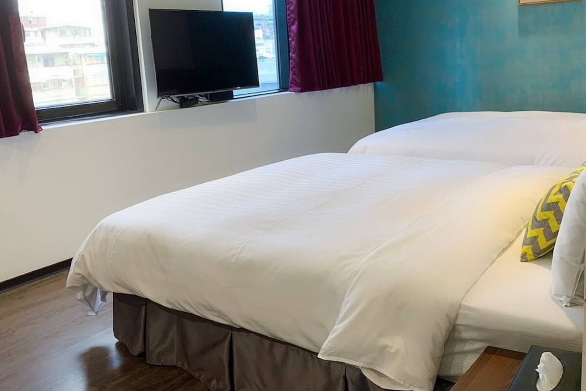 A hotel room with a large bed, a TV on the wall, and a window with curtains.