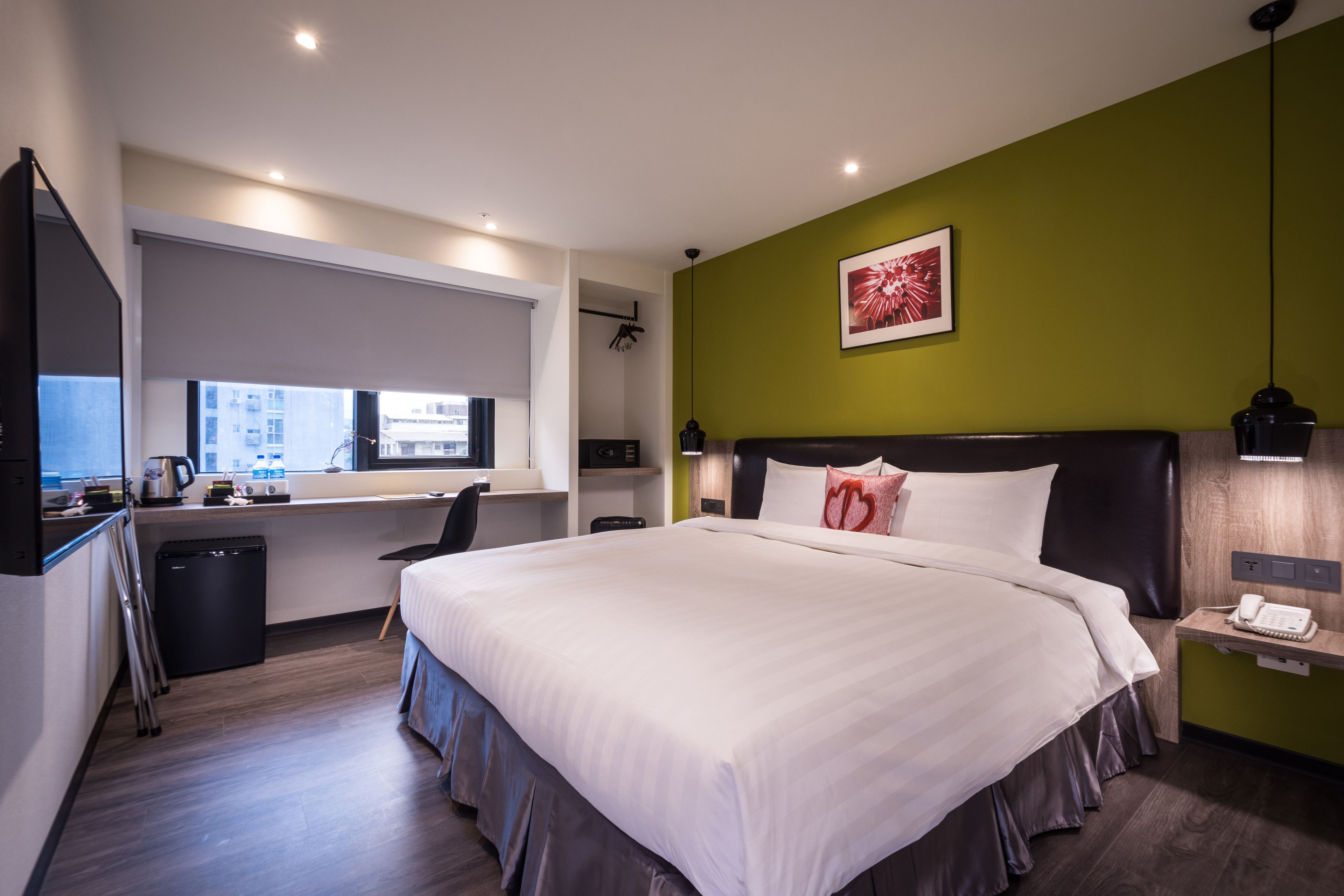 A modern hotel room with a large bed, a desk, and a window with a city view.