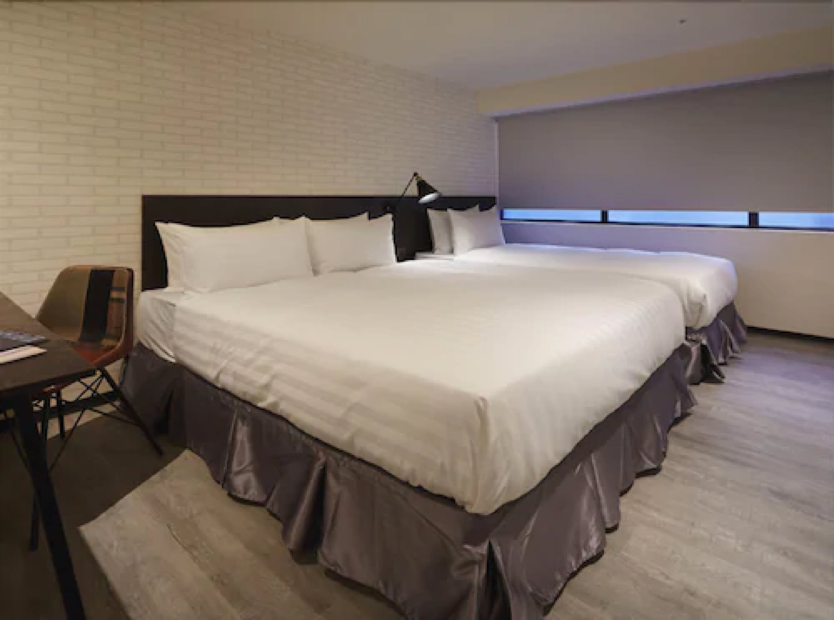 A hotel room with two beds, a desk, and a chair.