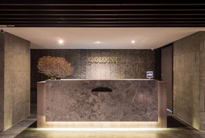 A reception desk with a dark marble top, a sign reading "GOLDIN", and a small digital screen. - Goldinn Hotel (Taipei)
