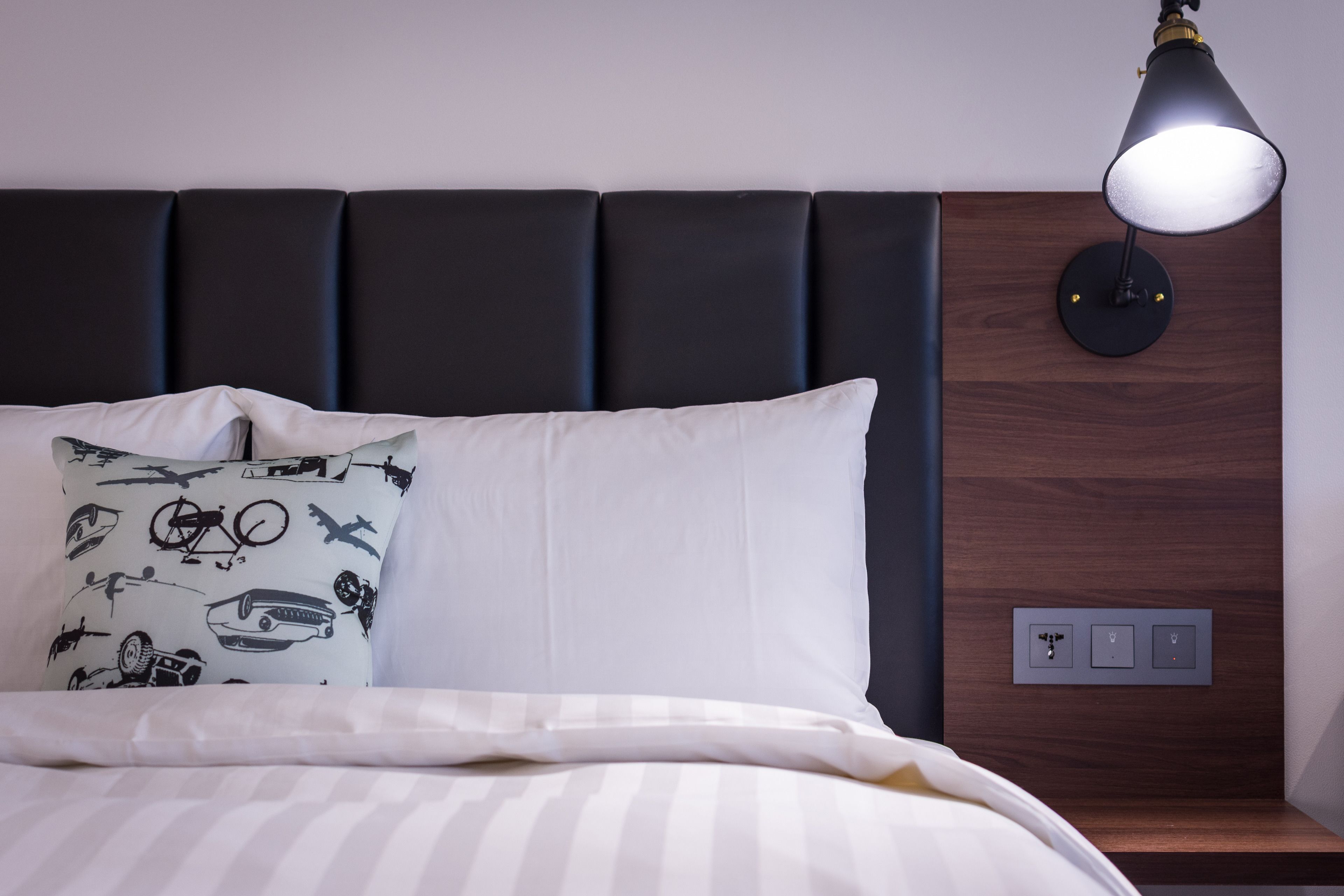 A neatly made bed with white and striped bedding, a black headboard, and a wall-mounted lamp.