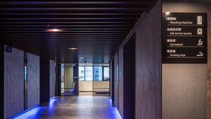 A modern hallway with a vending machine, self-service laundry, a gymnasium, and a smoking area. - Goldinn Hotel (Taipei)