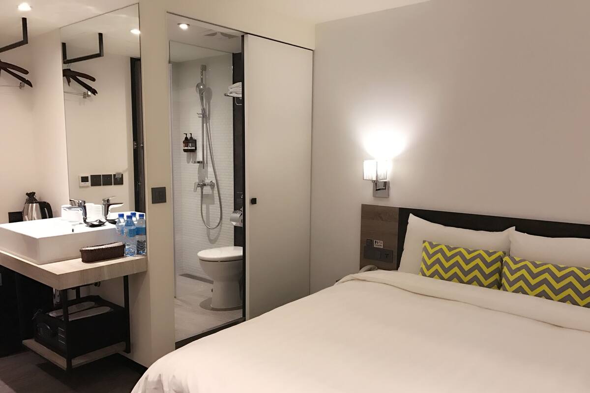 A hotel room with a bed, a bathroom with a shower, a sink, and toiletries.
