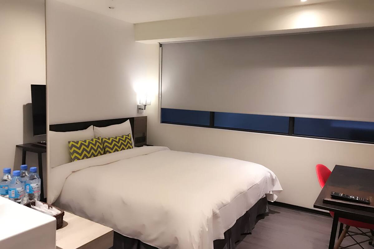 A hotel room with a bed, a desk, a chair, a TV, and a window.