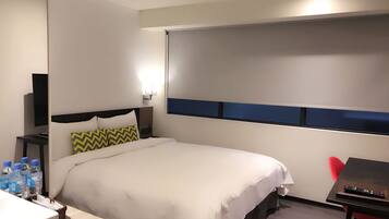 A hotel room with a bed, a desk, a chair, a TV, and a window.