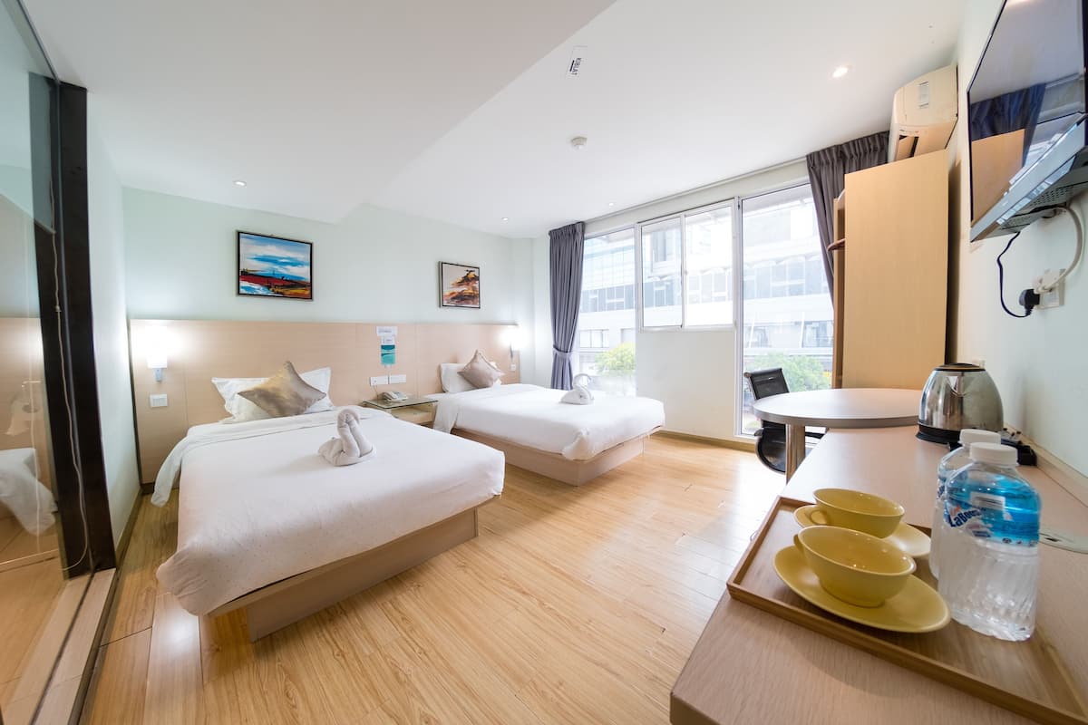 A hotel room with two beds, a dining table, a kettle, and a tray with cups and a bottle.