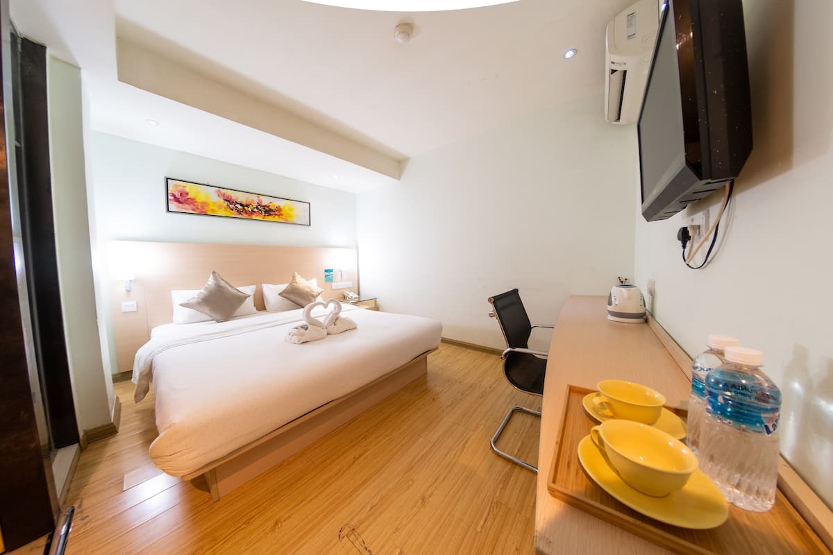 A hotel room with a bed, a desk with a chair, a TV, and a painting on the wall.