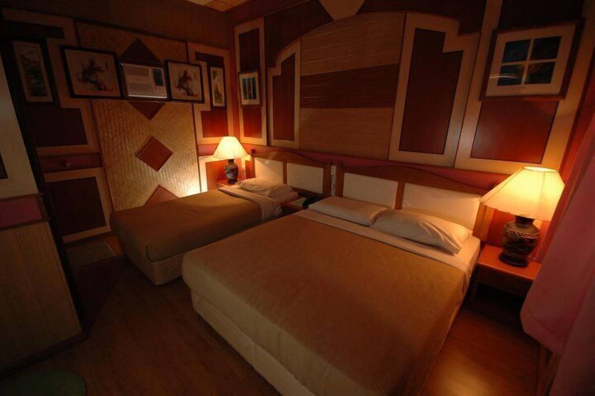 A hotel room with a large bed, a smaller bed, and two bedside tables with lamps.