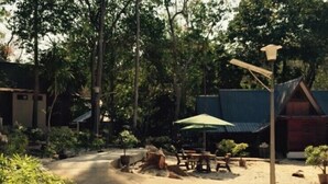A pathway leading to a seating area with tables and chairs, surrounded by greenery and buildings with thatched roofs. - Shari-La Island Resort (Pulau Perhentian Kecil)