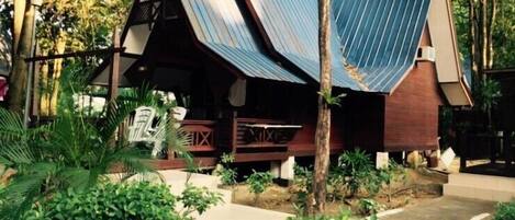 A rustic wooden structure with a sloped roof, surrounded by lush greenery and trees.